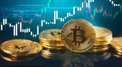 Auf diesem Bild sind einige Bitcoin Münzen zu sehen. Im Hintergrund sieht man einen Chart auf blauem Hintergrund.